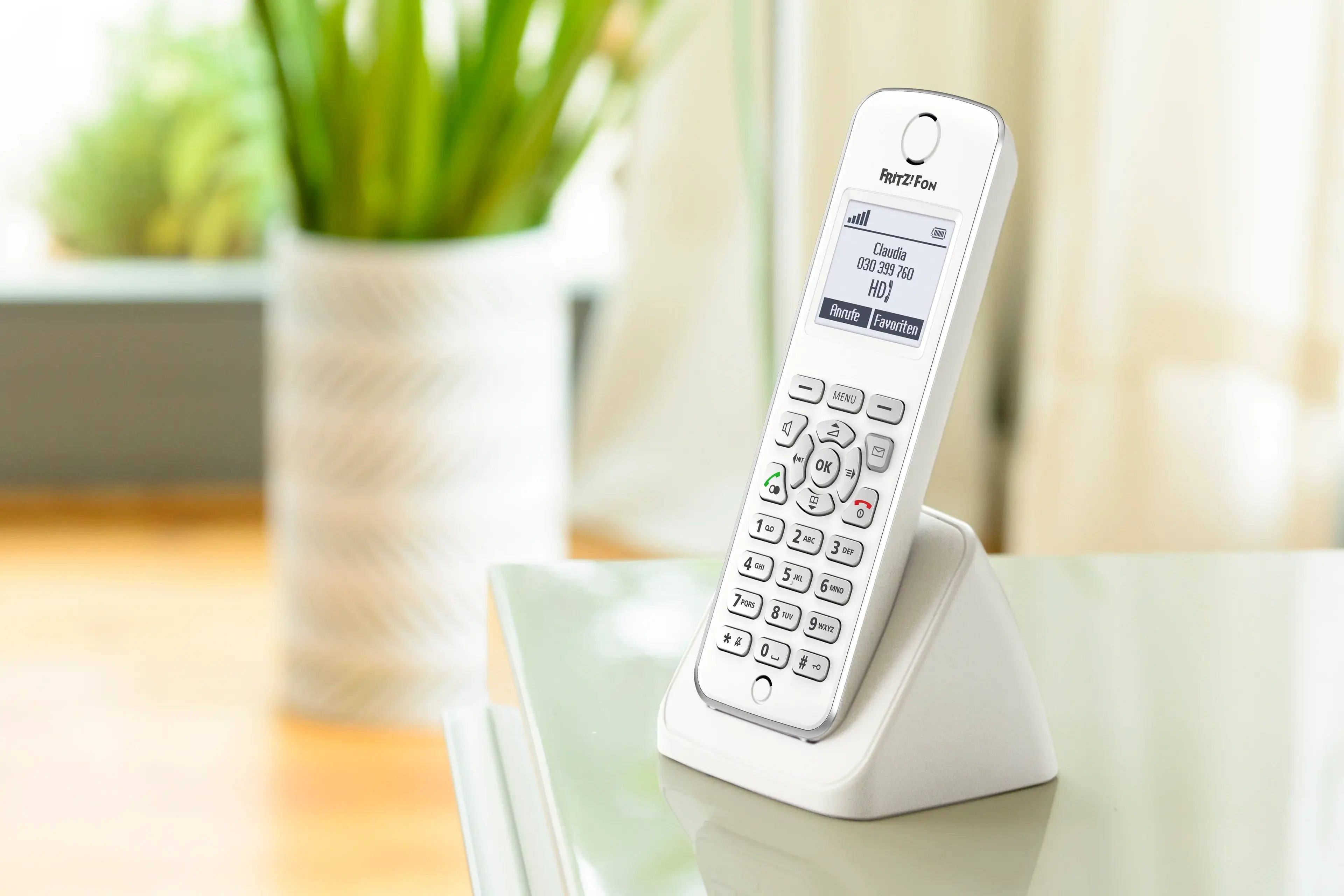 Weißes Festnetztelefon auf Tisch mit grünem Pflanzenhintergrund, ideal für Heimtelefonie.